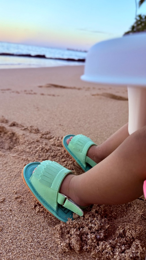 Gia's mint green sandals in the sand at sunrise, ocean behind her