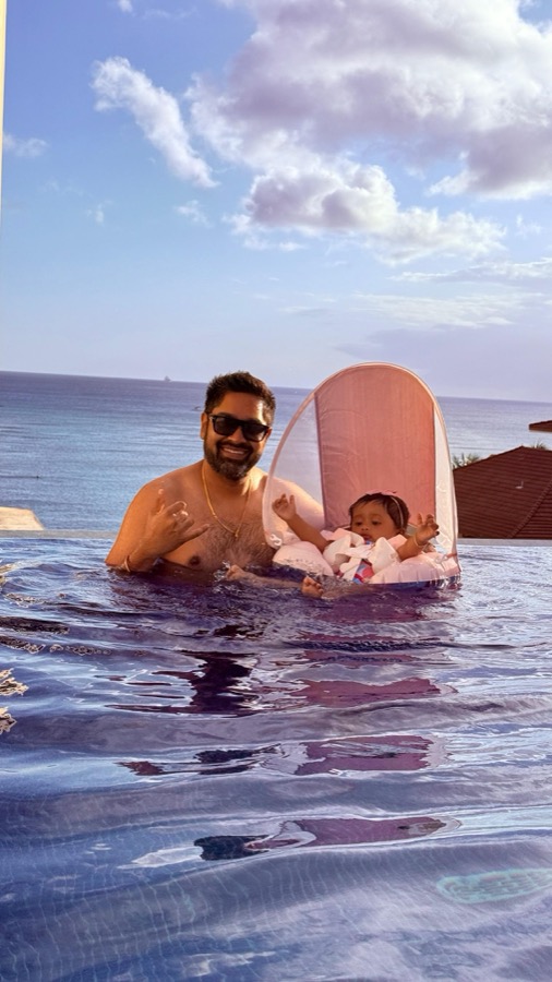 Gautam in the Halepuna infinity pool with Gia in her floater, Pacific Ocean behind them