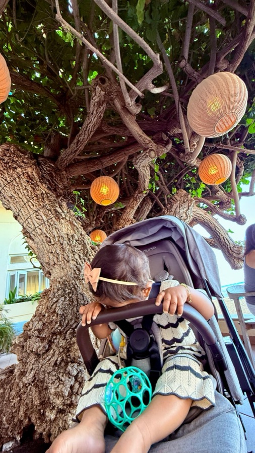 Gia face down on her stroller bar at Hau Tree, the famous banyan tree with lanterns behind her