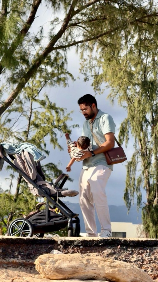 Gautam holding Gia in one arm and Kanak's Burberry bag on the other shoulder